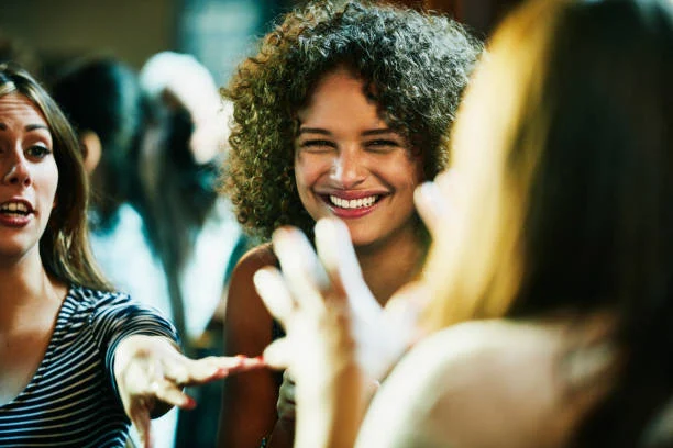 Flera personer, inklusive una kvinna med mörkt lockigt hår, skrattar under ett språkcafé.